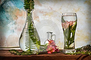 Cut flowers and tropical plants in a glass of water on a barn wood table