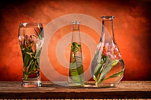 Cut flowers and tropical plants in a glass of water on a barn wood table