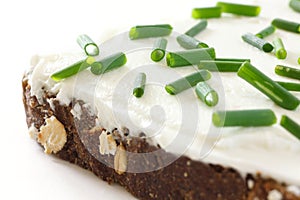 Cut fresh chives on thickly spread cream cheese on dark health bread photo