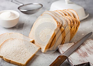 Cut of fresh loaf of white bread with flour and butter on light kitchen table background with chopping board and bread knife.