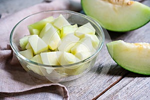 Cut of fresh sweet green melon in bowl glass on the wooden background. Fruits or healthcare concept. Selective focus, close up