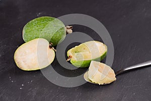 Cut fruit of the mature feijoa on a dark slate background. Pulp fruit on the bark spoon