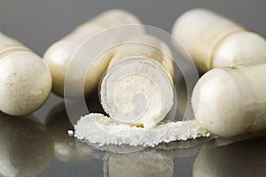 Cut glucosamine capsules, food supplement pills on glossy dark background, macro image.