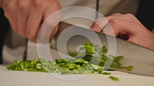 Cut the green onions with a knife on the board. Cutting green without hands in the frame. Chef cuts the ingredients for