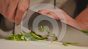 Cut the green onions with a knife on the board. Cutting green without hands in the frame. Chef cuts the ingredients for