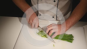 Cut the green onions with a knife on the board. Cutting green without hands in the frame. Chef cuts the ingredients for
