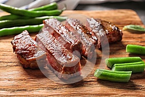 Cut grilled steak with green beans on wooden board