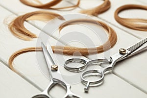 Cut hair curls and thinning scissors on a white wooden background