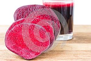 Cut half beetroot and fresh beet juice in glass on wooden table, white background.