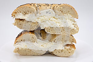 A Cut in Half Large Poppy Seed Bagel filled with Cream Cheese on a White Plate with a White Background