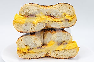 Cut in Half and Stacked New York Style Toasted Sesame Seed Bagel with Bacon Eggs and Cheese on a White Plate