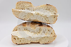 Cut In Half Toasted Sesame Seed Bagel with Cream Cheese on a White Plate with a White Background