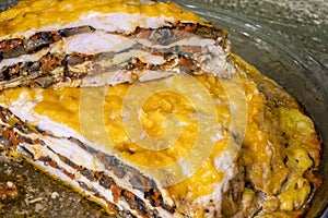 Cut Layered baked meat pie with mushrooms and vegetables covered with melted cheese is on the table in glass tray