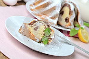 Cut of marble cake sprinkled with sugar, lemon, melissa, milk, eggs and butter