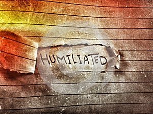 On a cut notebook page the word humiliated written