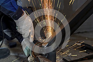 Cut-off male hands of worker hold grinding machine from under which sparks of molten metal fly.