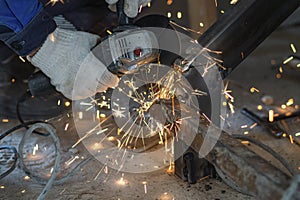 The cut-off male hands of a worker hold a grinding machine from under which sparks of molten metal fly. Welding job.