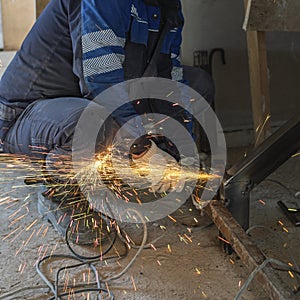 The cut-off male hands of a worker hold a grinding machine from under which sparks of molten metal fly. Welding job.