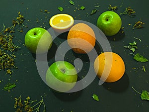 Cut orange and apple on a dark background. Around the herbs still life close up