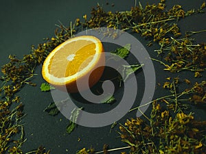 Cut orange on a dark background. Around the herbs still life close up