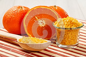 Cut orange, wooden spoon and glass bowl with yellow sea salt