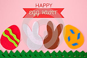 Cut out of felt applications of eggs and white and brown rabbits on the grass. Pink background. Flat lay. Easter holiday