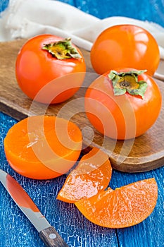 Cut persimmon fruits on wooden board and table, vertical