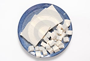 Cut into pieces and cubes of tofu on a blue plate close-up on white background.