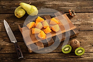 Cut into pieces orange hurma using a knife on a wooden cutting board photo