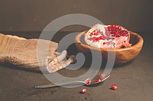 cut into pieces red garnet in a wooden bowl on the table/parts of pomegranate in a wooden bowl and a spoon against a dark
