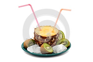 Cut pineapple with two pink tubes on a green plate, surrounded by a kiwi cut in half and ice cubes