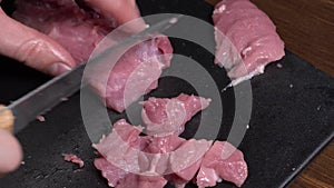 Cut pork or beef meat with a knife on the table close-up. Preparation of meat dishes and food. Chunks of red meat.