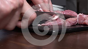 Cut pork or beef meat with a knife on the table close-up. Preparation of meat dishes and food. Chunks of red meat.