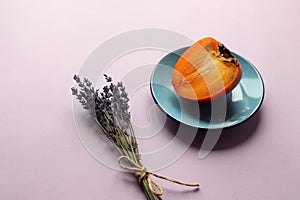 Cut ripe persimmon fruit on a blue plate, lavender bouquet, pastel background, side view - the concept of the usefulness of