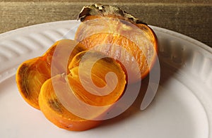 Cut ripe persimmons on a white plate with a hard dry calix attached.