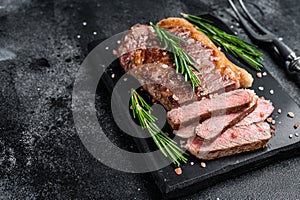 Cut roasted new york strip beef meat steak or striploin on a marble board. Black background. Top view. Copy space