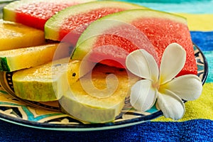 Cut slices of red and yellow watermelon decorated with a Plumeria or Frangipani flower on a colorful patterned ceramic plate