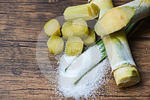 Cut sugar cane piece and white sugar wooden background top view