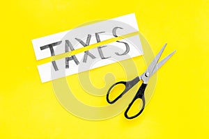 Cut taxes concept. Sciccors cut paper with word Taxes on yellow background top view space for text