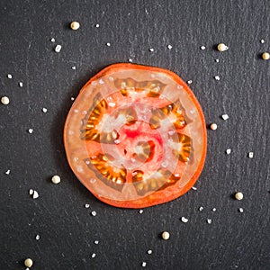 Cut tomato red with seeds and patterns. View from above. Black stone slate background.