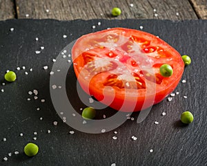 Cut tomato red with seeds and patterns. View from above. Black stone slate background.