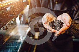 Cut view and close cup of man holding coffee beans in hands. He stands at coffee machine.