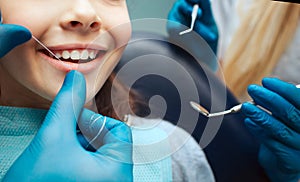 Cut view hands in latex gloves to floss child front teeth. Woman hold dental tools beside.