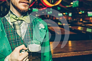 Cut view of man in green saint patrick`s suit stand in pub and hold mug of beer. Guy is alone in room.