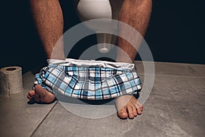 Cut view of man`s hairy legs with briefs on feet. Man sit on pot in wc or toilet. Doing defecation. Alone in rest room