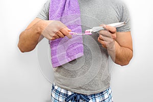 Cut view of man standing and putting tooth paste onto tooth brush. He has violet towel on shoulder. He stands in pijamas