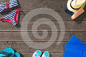 Cut view of summer clothing. Hat. Female swimming suit. Flip flops. Fins. Sun protecting cream in orange bottle. Wood