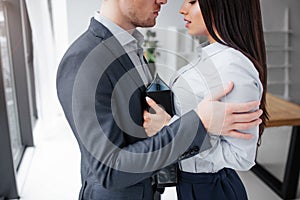 Cut view of young man and woman standing very close to each other. He embrace her. She looks down and hold black folder