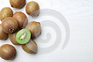 Cut and whole fresh kiwis on white wooden table, flat lay. Space for text