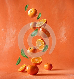 Cut and whole ripe mandarine with leaves falling in the air on an orange background. Levitating tangerines in the air